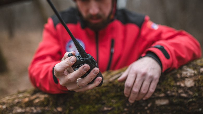 Hiker, leaning on tree log, holding walkie-talkie