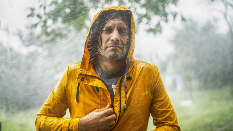 Unhappy man zipping up jacket in heavy rain