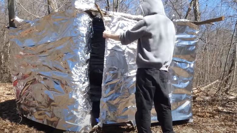 Man wrapping shelter with aluminum foil