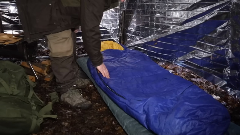 Man laying out sleeping bag inside foil-wrapped tent