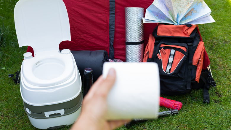 Handing holding toilet paper in front of portable toilet and camping gear