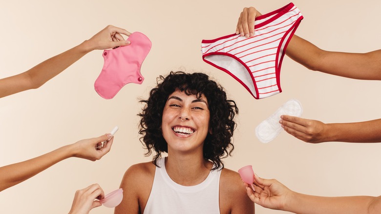 Smiling woman surrounded by hands holding a variety of menstrual products