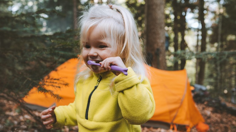 Child brushing teeth outdoors in front of camping tent