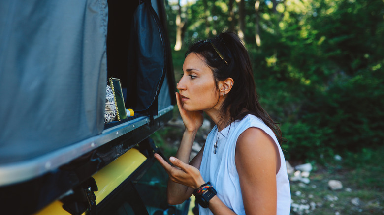 Woman putting on skincare and makeup through small mirror in tent