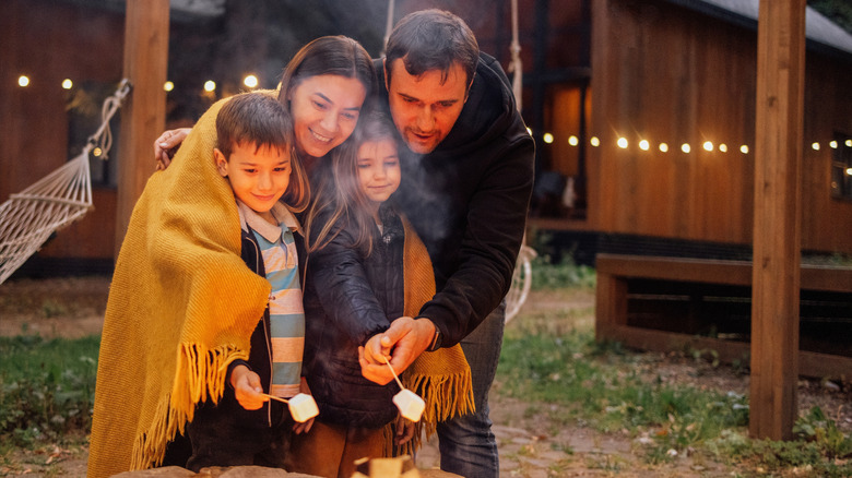 Family cuddled up in blanket roasting marshmallows by campfire