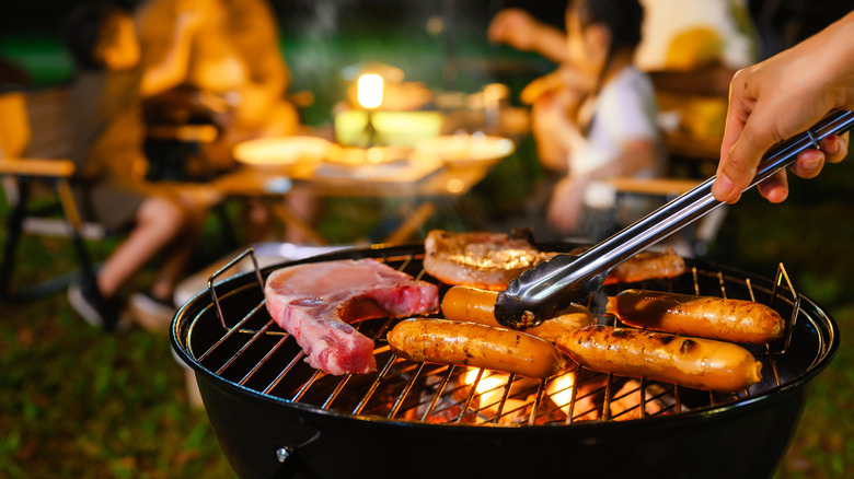 Closeup of food cooking on campfire grill with family in background