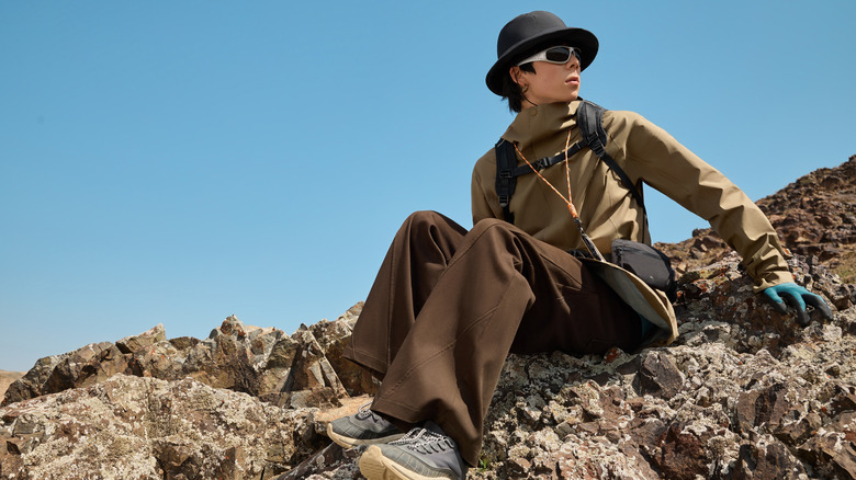 Stylish hiker sitting on rock, looking on