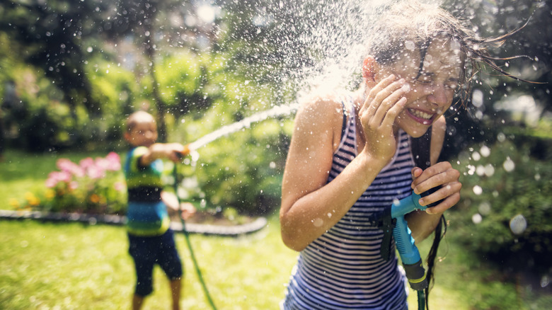 Boy spraying water at girl with hose