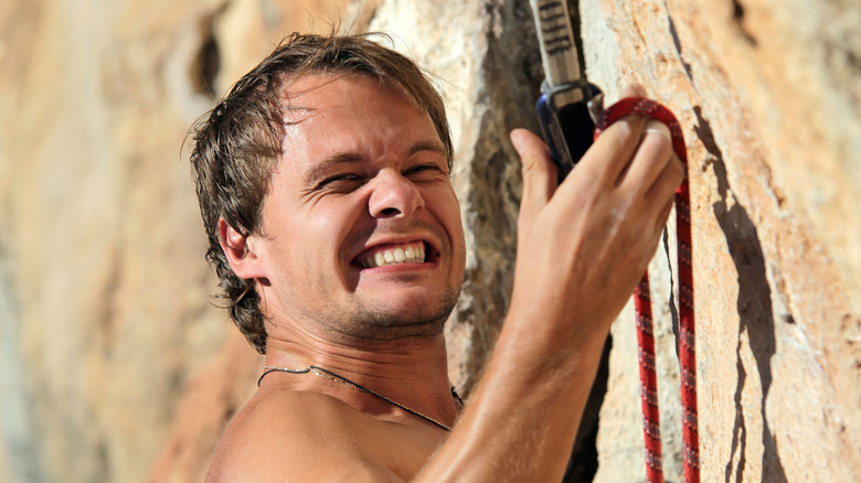 Man struggling to clip in while rock climbing