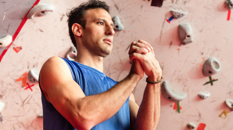 Man warming up wrists in front of indoor rock wall