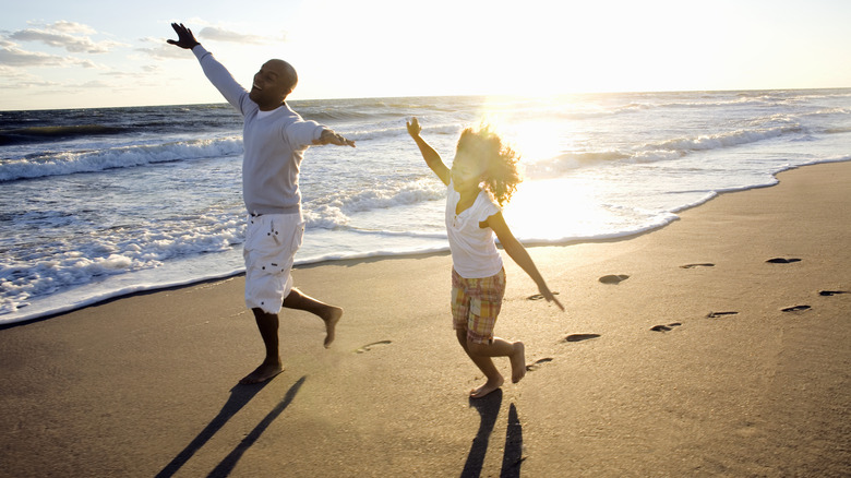 Two people running on a beach with the sun behind them