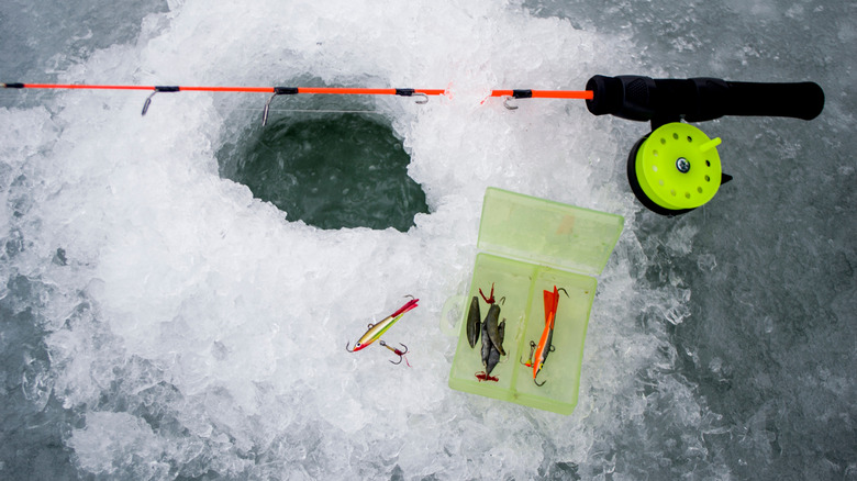 Ice fishing tackle next to ice fishing hole and rod