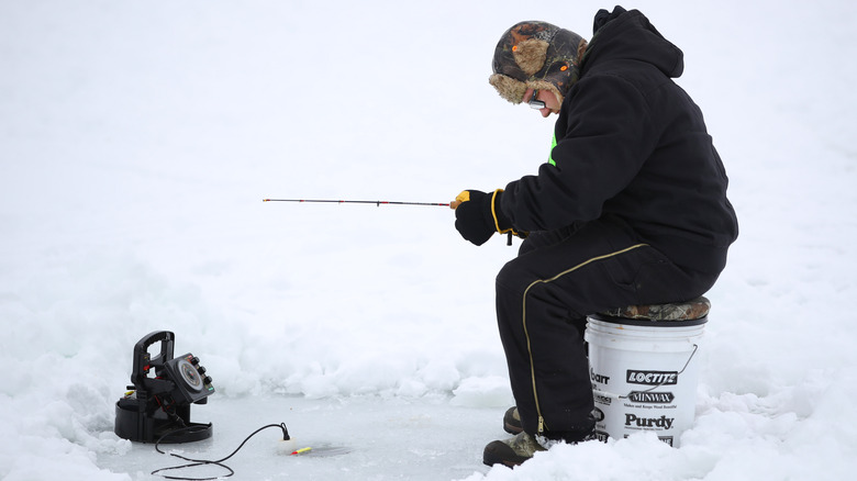 Man seated on bucket, ice fishing