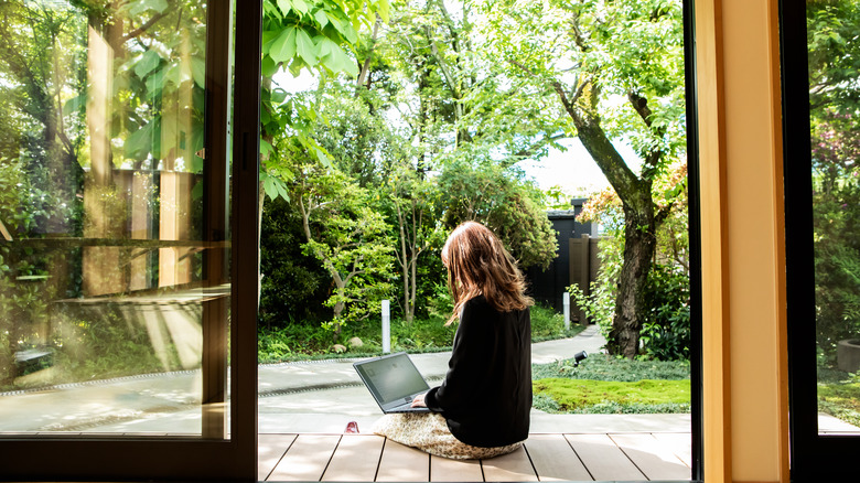 Woman using laptop on patio, surrounded by trees