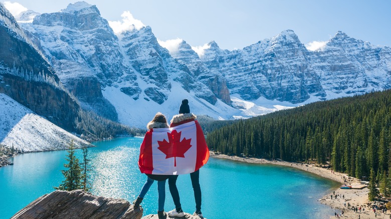 Pair of travelers draped in Canadian flag in front of Moraine Lake