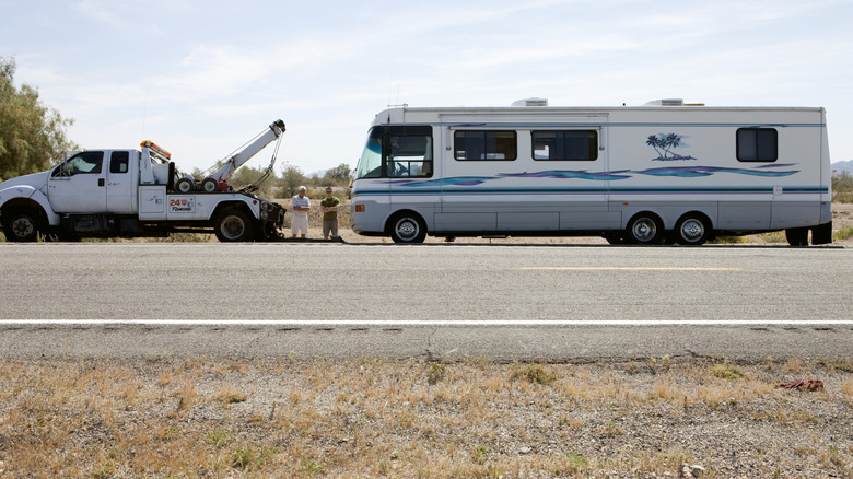 Two men standing roadside with tow truck and RV