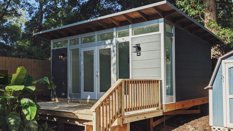 A lifted shed with a porch and stairs in a backyard