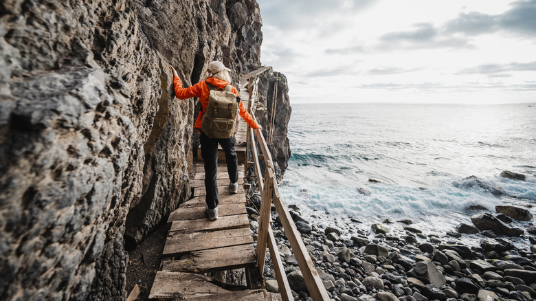 Woman on broken cliffside boardwalk by ocean