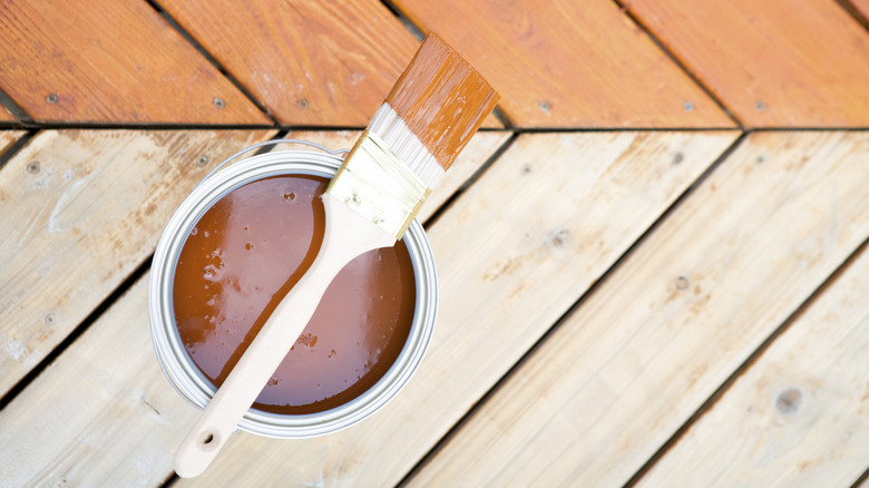 Half-stained wooden deck, stain in can, and paintbrush