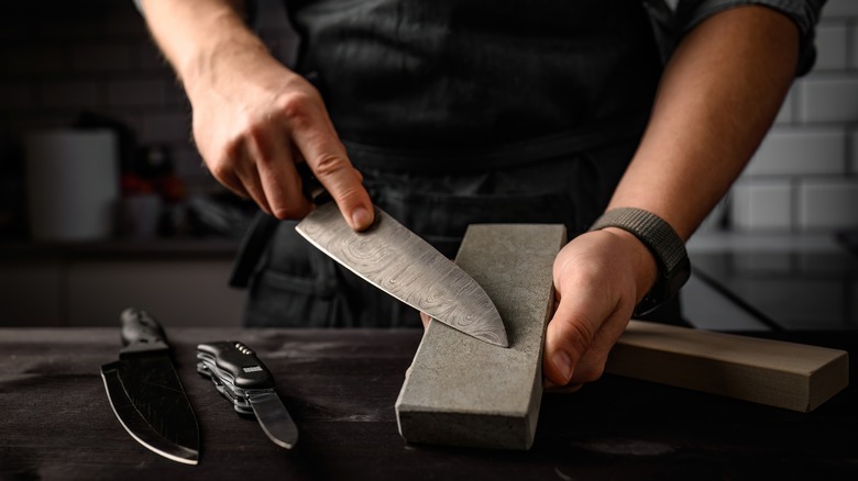 Pair of hands sharpening knife with a grindstone