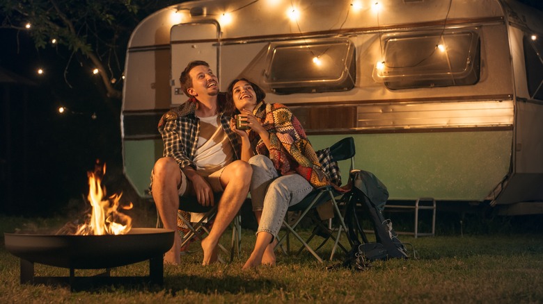 Couple sitting by campfire next to RV at night