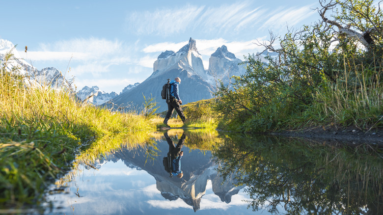 Hiker walking along river with forest and mountains in background