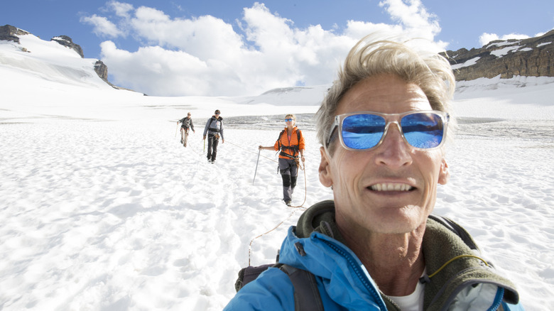 Winter hiker wearing sunglasses, taking selfie with hikers in background