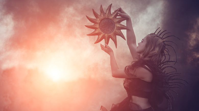 Fantastical woman holding model of sun up to the sky
