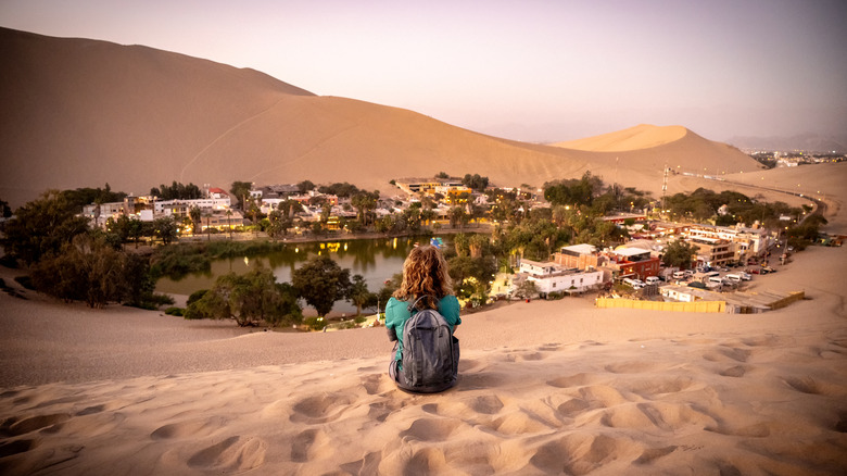 Woman with backpack sitting on sand dunes overlooking Huachina oasis