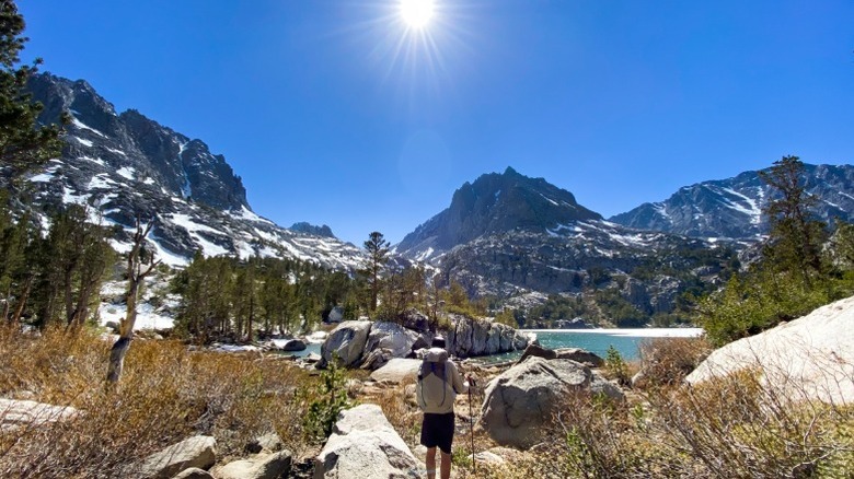 A man hiking in the mountains facing the sun, which is high in the sky