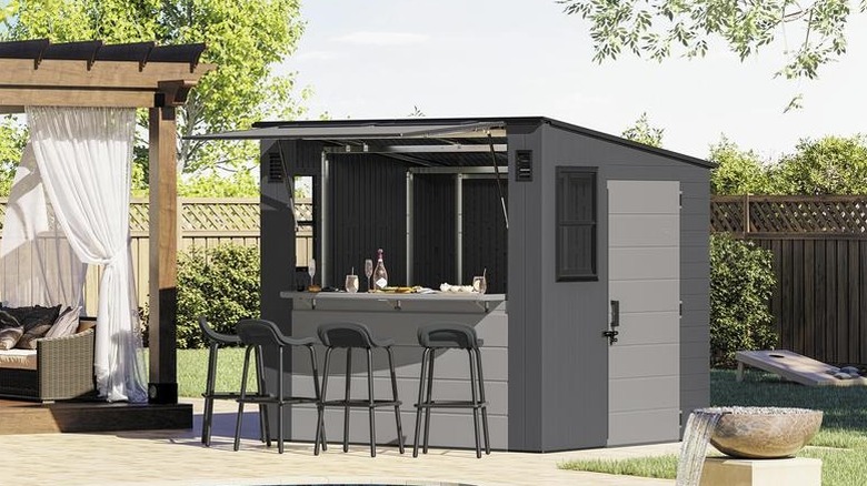 The Suncast Entertainment Shed in a backyard with the canopy open, and four benches placed in front of it