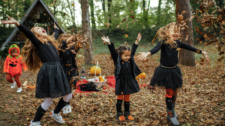 Kids in Halloween costumes playing with leaves outside of cottage