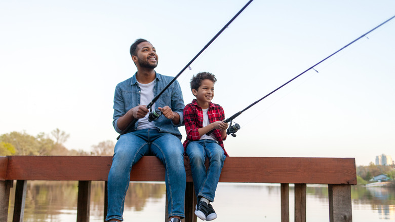 Father and son duo fishing together, seated on dock