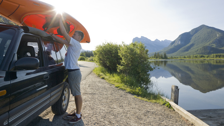 Man loading kayak on top of vehicle