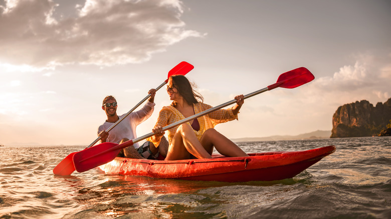 Two smiling people paddling in a tandem kayak