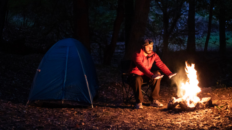 Man seated near campfire and tent