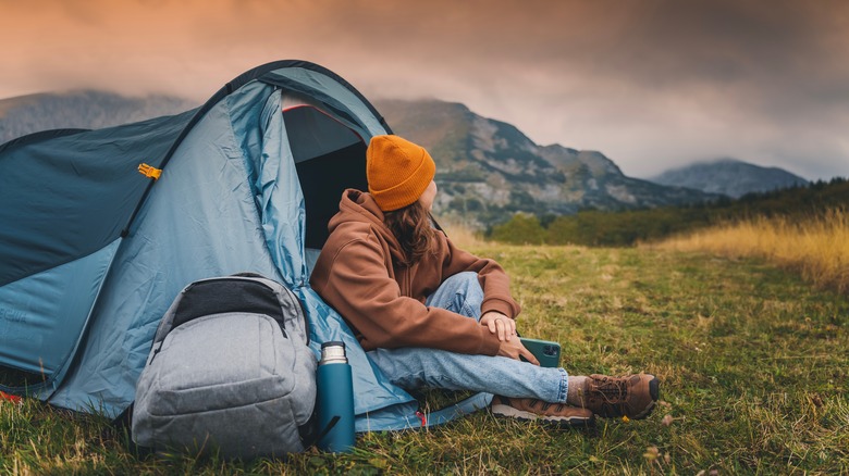 Camper sitting in front of tent looking out of it into the distance