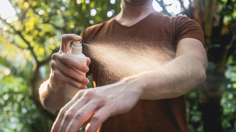 Person spraying mosquito repellent on arm