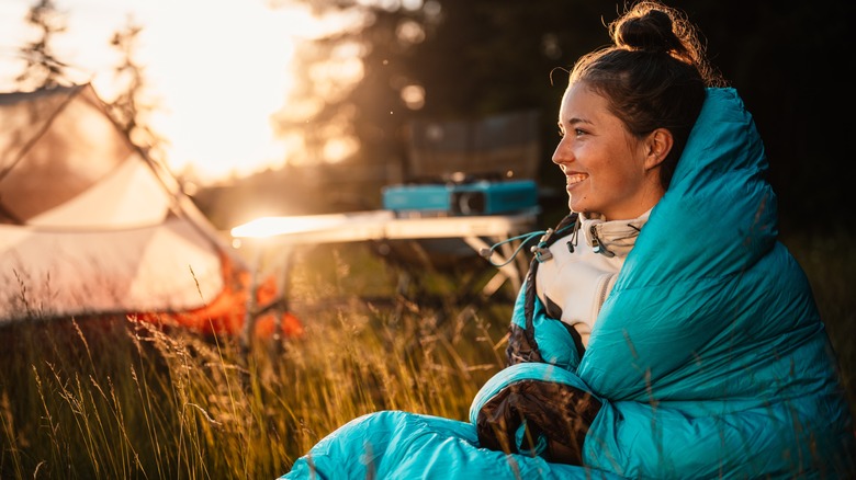 Young woman enjoying sunrise in a sleeping bag