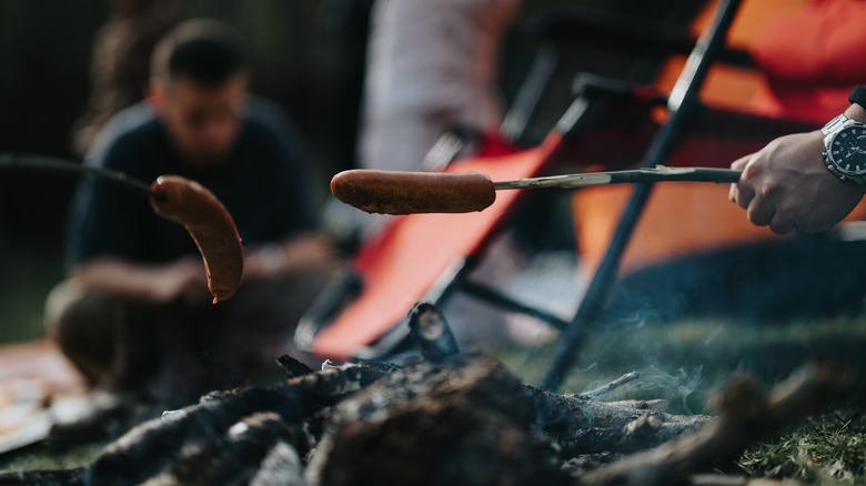 cooking hot dogs over fire with stick