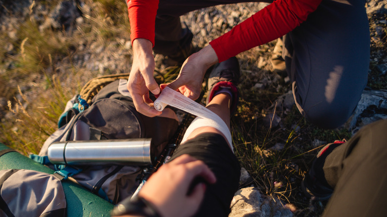 Person helping fellow hiker put bandage on leg