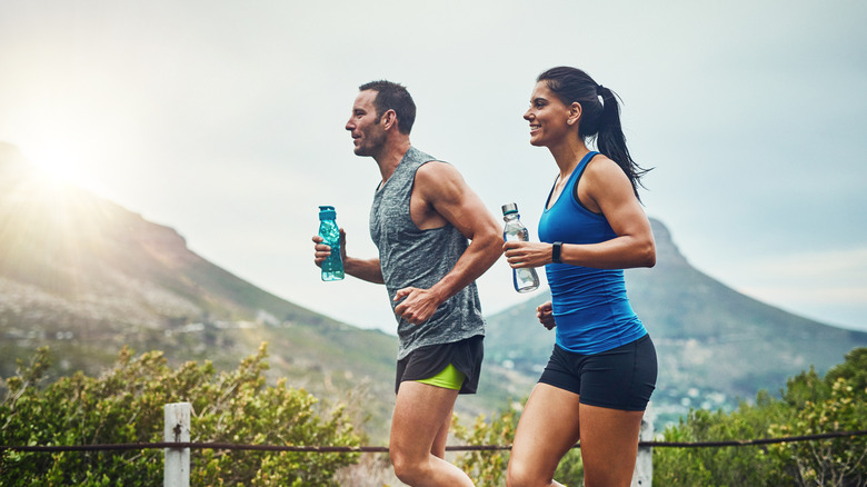 Couple jogging together outside, carrying water bottles