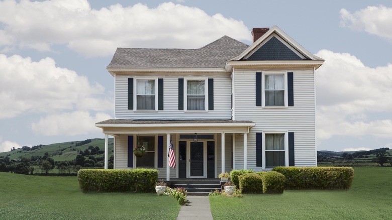 A beautiful white home on a flat, green lawn with bushes around the home and clouds in the background