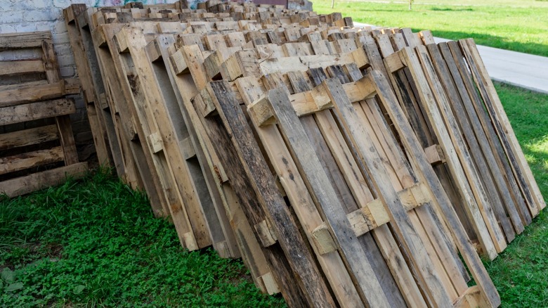 A bunch of old wood pallets stacked outside against a wall.