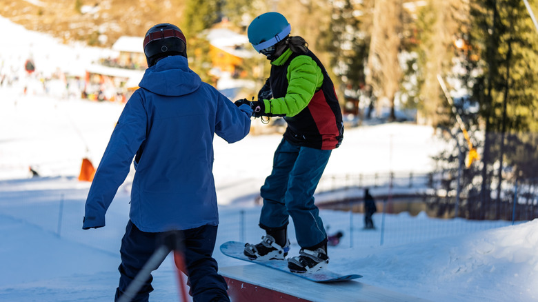 A child learning to snowboard with an instructor