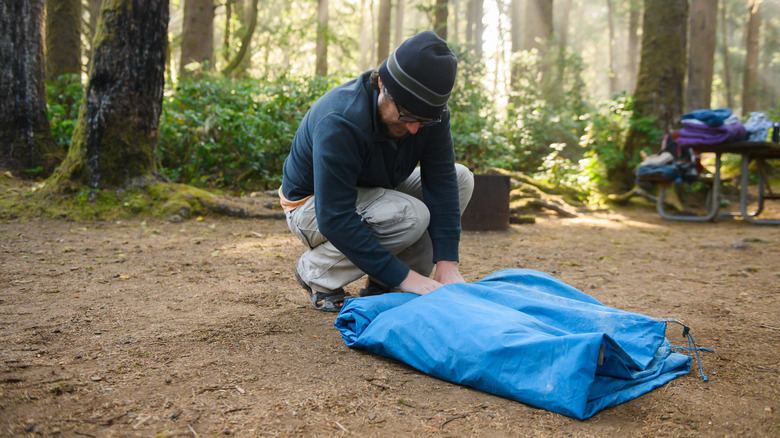 Man rolling tent in woods