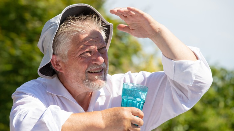 Man holding glass of water, shading himself from sun with hand