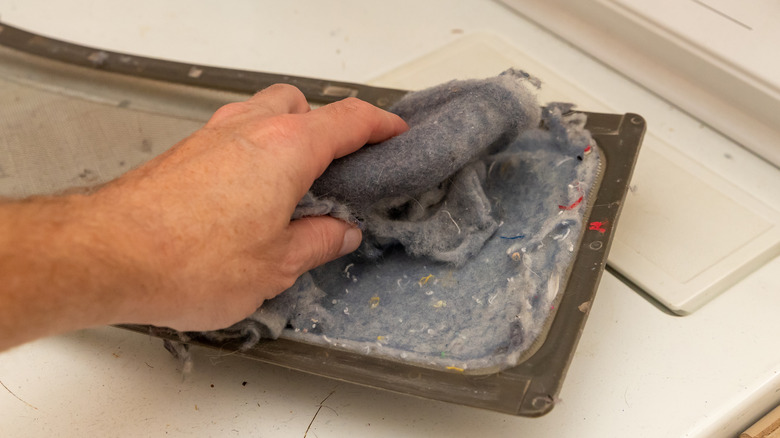 Hand scraping dryer lint from laundry dryer's lint trap