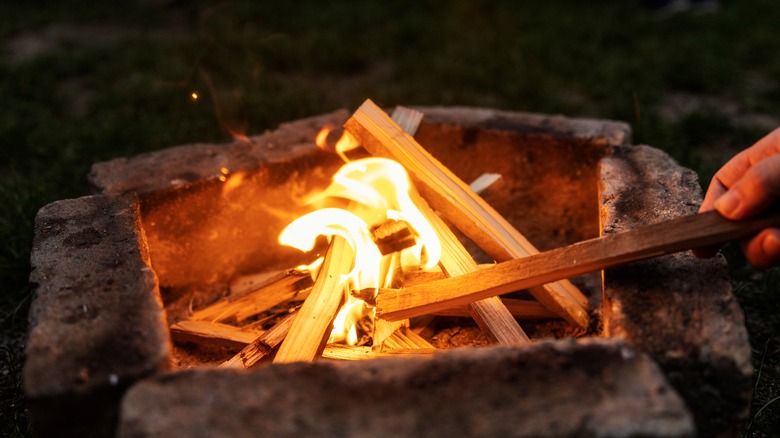 Hand poking campfire with stick