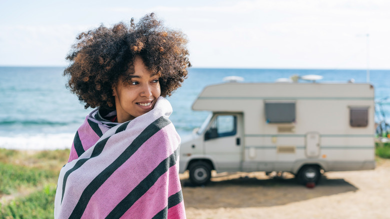 Woman wrapped in colorful towel with an RV and the shore behind her